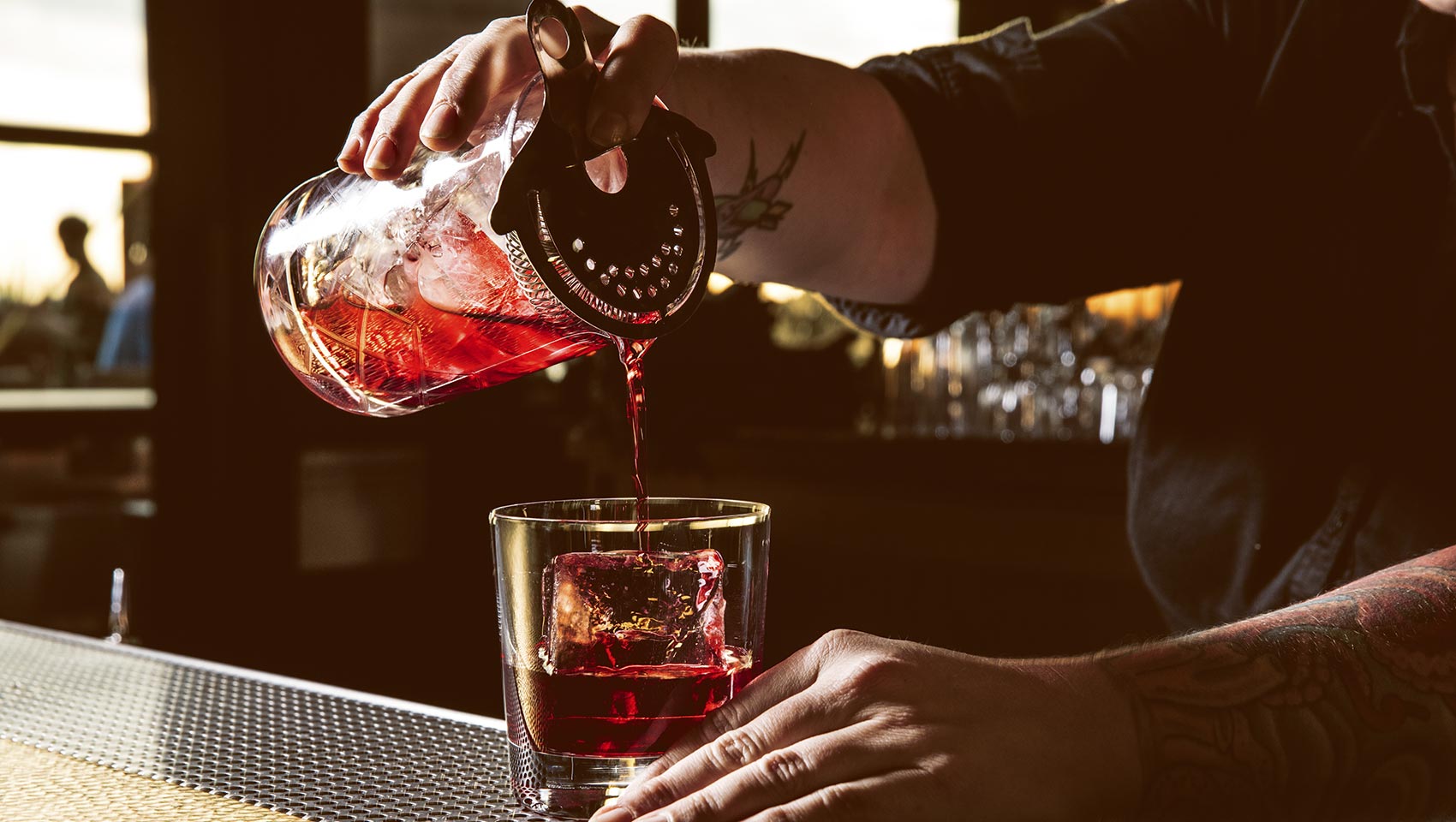 handsof a bartender pours a cokctail into a glass with ice