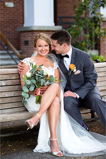 Bride and groom sit on bench while groom smiles at bride and she smiles at the camera at Kimpton River Place Hotel