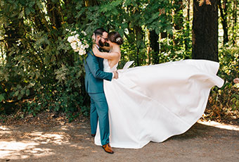 bride and groom hold eachother standing in front of greenery